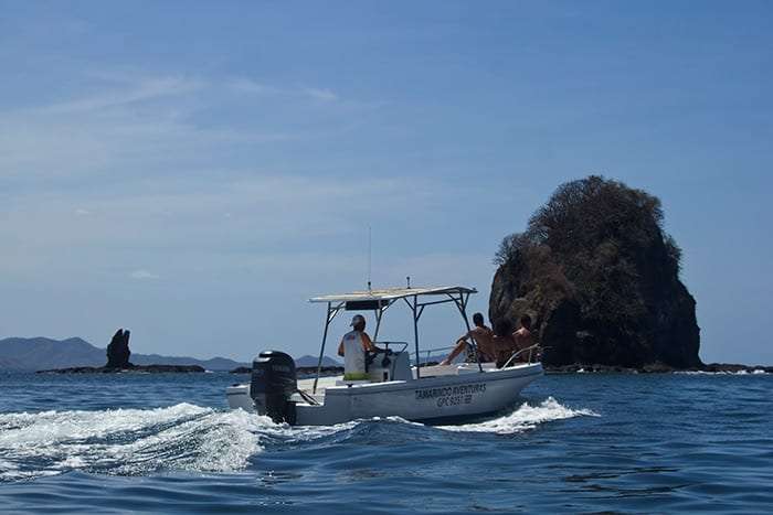 Small white boat with passengers heading toward a dark rock islet in the bay