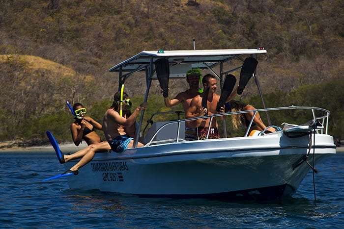 Snorkelers with fins sitting on a white boat anchored near a dry hillside