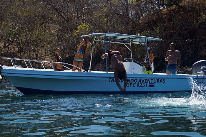 Man diving headfirst off the side of a white boat while others watch