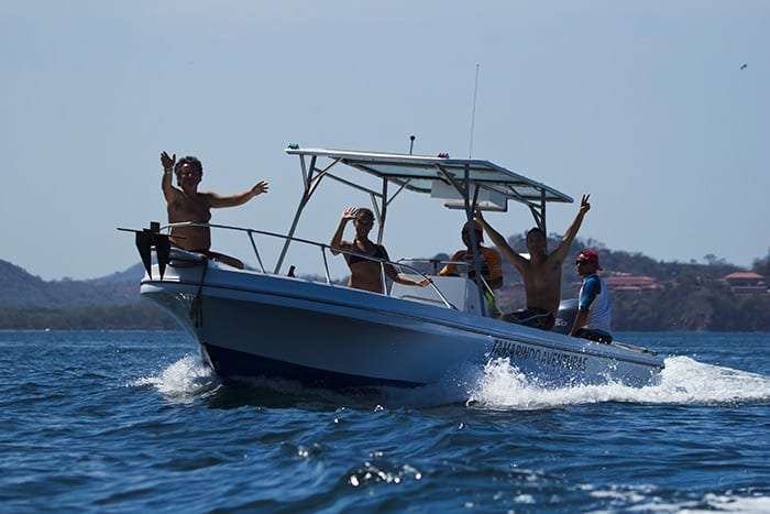 Passengers waving from a white boat speeding across the bay