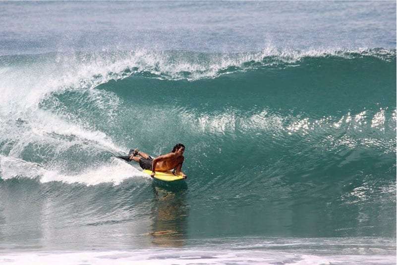 Bodyboarder lying on a yellow board riding inside a green barreling wave
