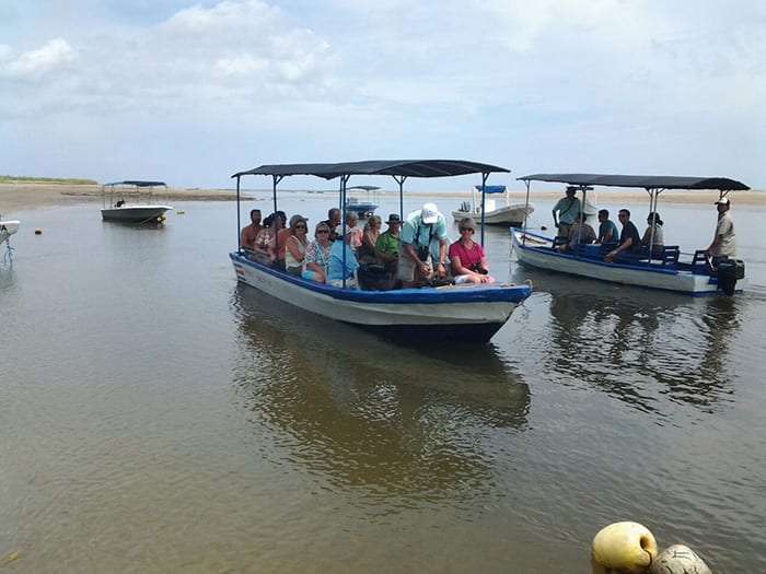 Two covered boats carrying passengers across a shallow estuary