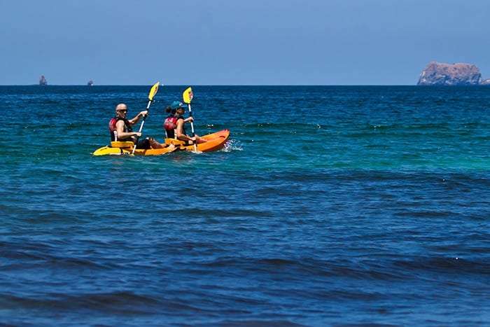 Tandem kayak on deep blue water with a small rock island in the distance