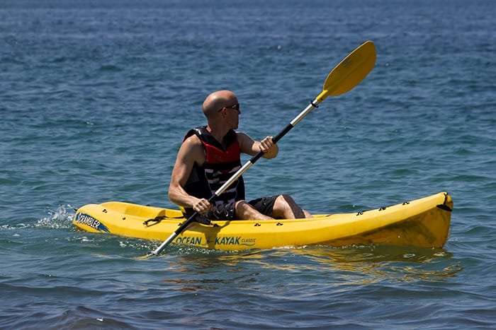 Man in a life vest paddling a yellow kayak on the sea