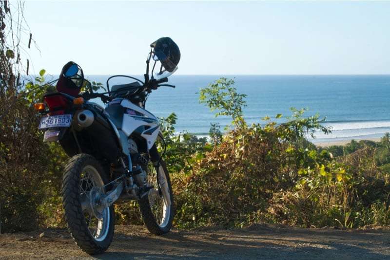 Dirt motorcycle with helmets hanging on the mirrors parked on a hilltop above the ocean