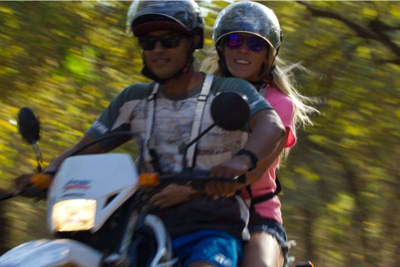 Man and woman in helmets riding together on a motorbike through blurred trees