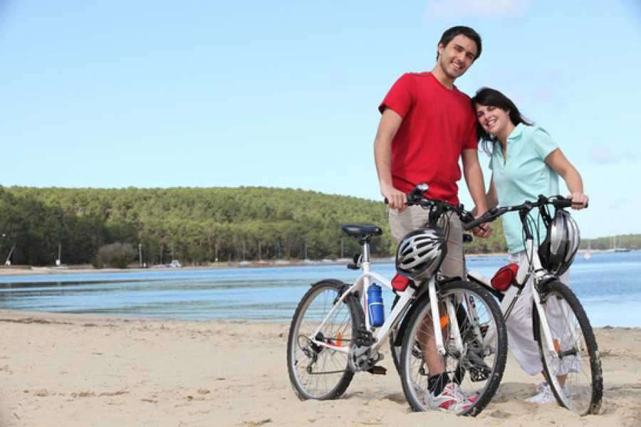 Smiling couple standing with two bicycles on a sandy lakeshore