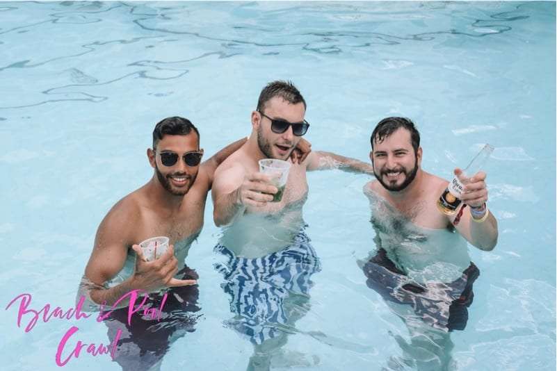 Three men in sunglasses standing in a pool holding drinks and a beer