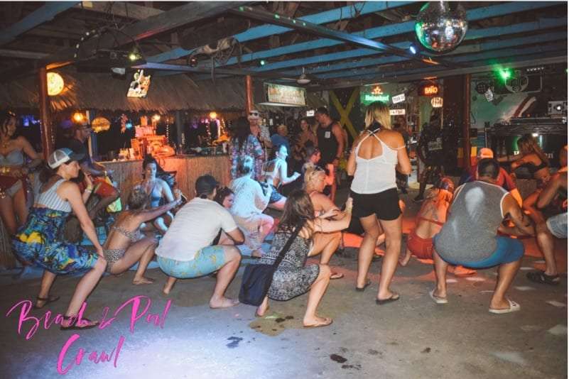 Group squatting and dancing on a bar floor under a disco ball at night