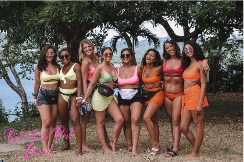 Group of women in bright swimsuits posing together under a tree above the water