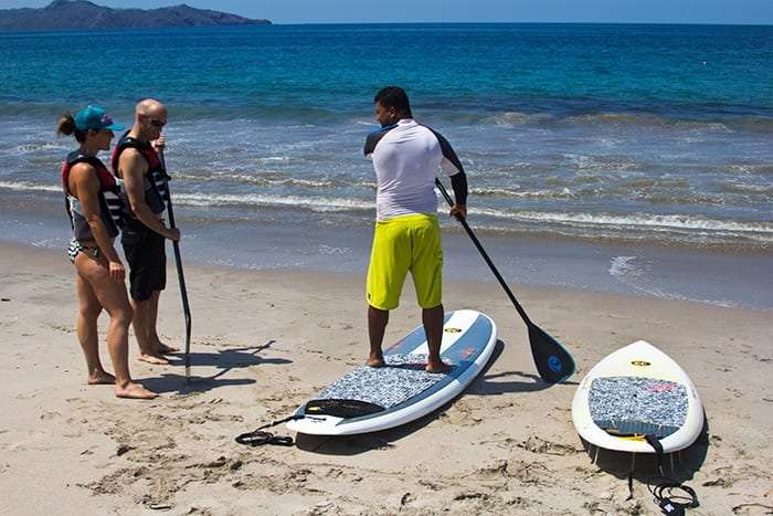 Instructor showing two people how to hold a paddle on a paddle board on the beach