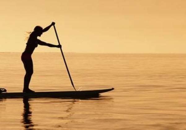 Silhouette of a woman paddling a stand-up paddle board on calm water at sunset