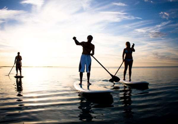 Three people on paddle boards on calm water at sunset