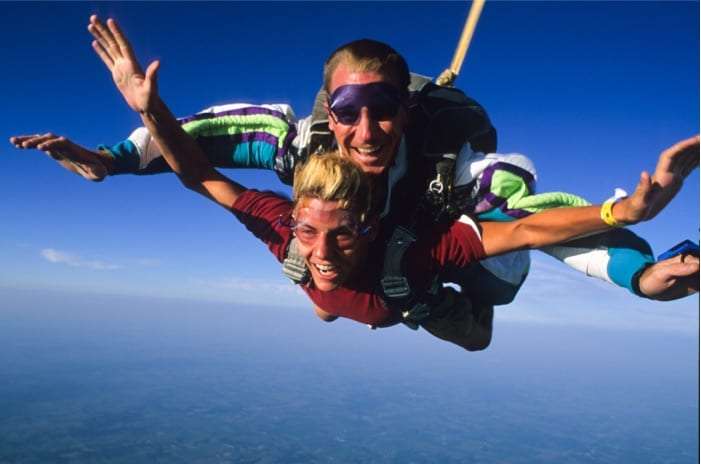 Two tandem skydivers smiling with arms spread in freefall