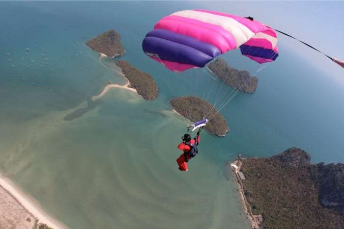 Skydiver with a pink and purple parachute above green islands and a turquoise bay