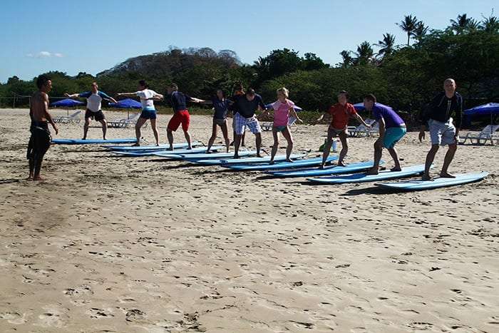 Students in a line standing in surf stance on boards on the sand with arms out
