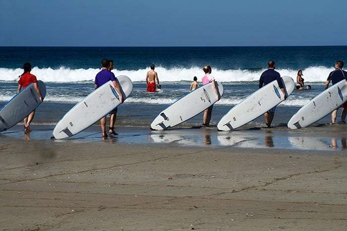 People carrying white surfboards toward the waves on a beach