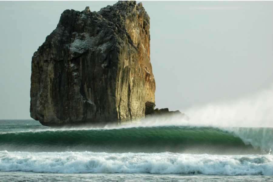 Rock formation rising from the sea beside a long green wave