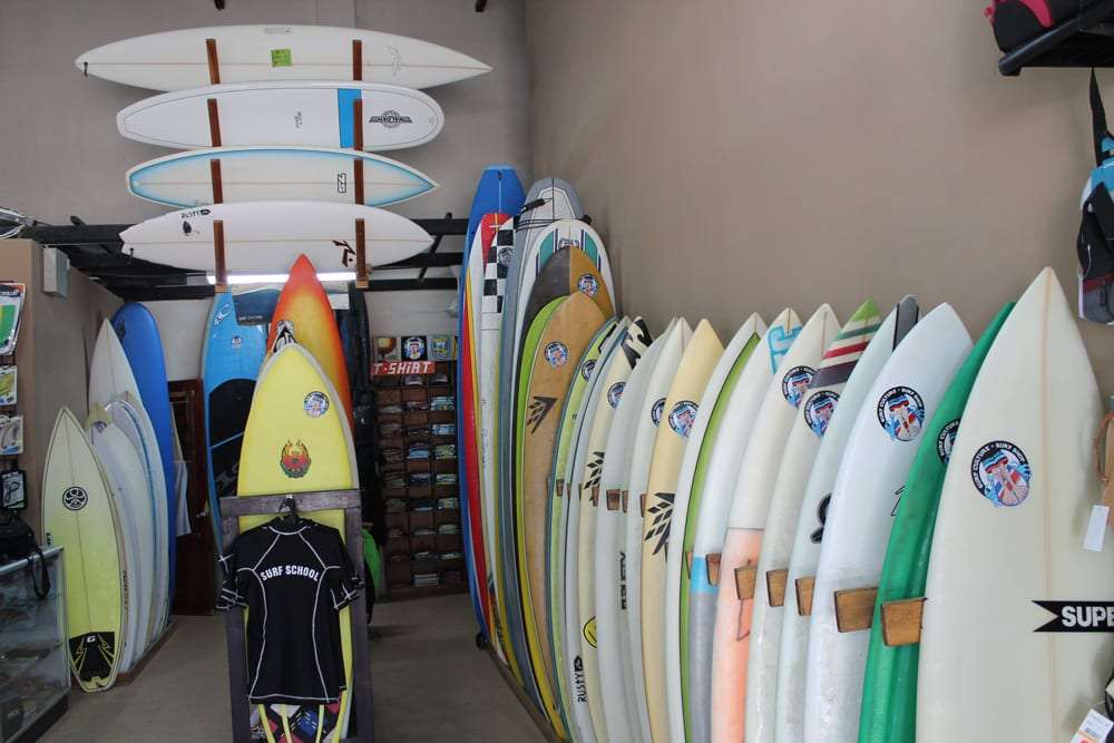 Surf shop interior with rows of surfboards and a surf school shirt on display
