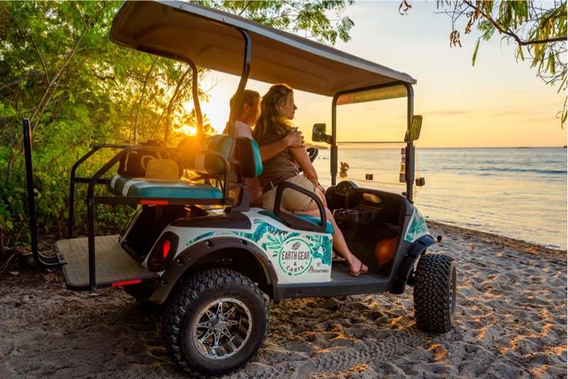 Couple sitting in a golf cart on a beach at sunset