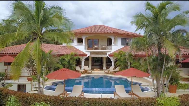 Villa with red umbrellas, sun loungers and a curved pool surrounded by palms
